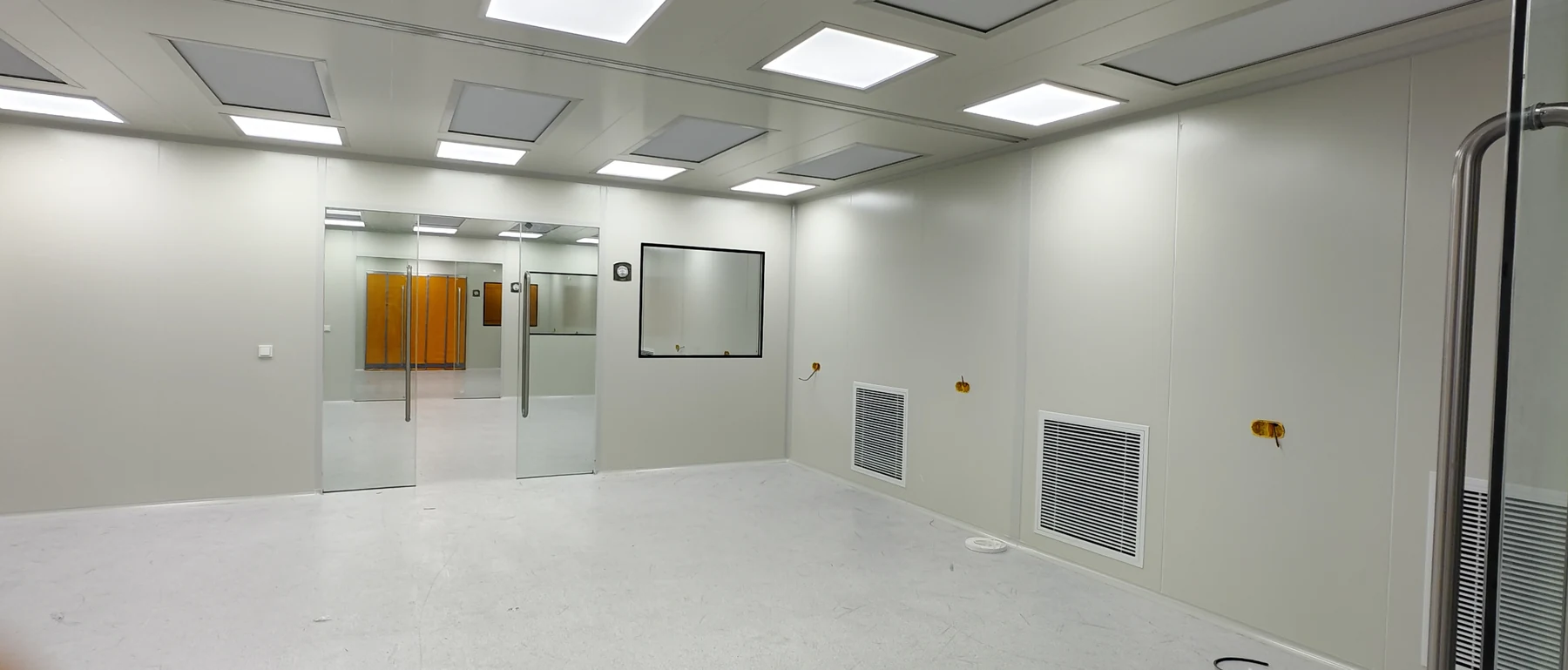 White cleanroom workshop with glass sliding doors, observation windows, ceiling air outlets and low-level return grilles during installation in Germany